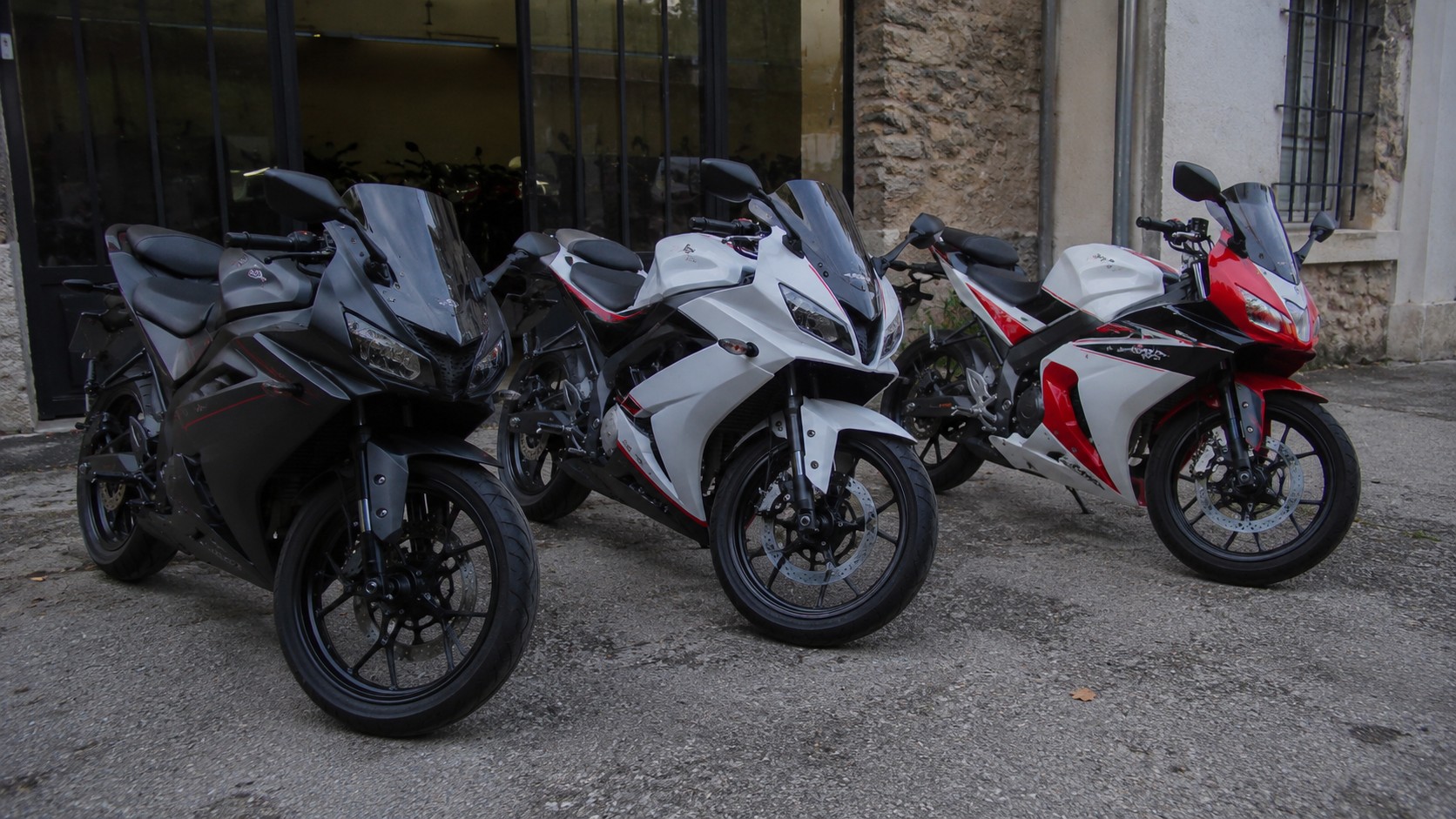 trois modeles de moto 50cc sportive carenee garees devant un garage
