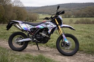 Moto 50cc type enduro avec kit déco holographique violet, bleu et noir, photographiée de profil sur un chemin en pleine campagne