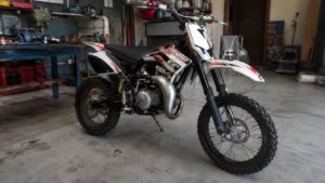 Beta 50cc rouge et blanche photographiée dans un atelier mécanique, avec moteur, échappement et roues tout-terrain visibles pour illustrer un avis sur la mécaboîte italienne.