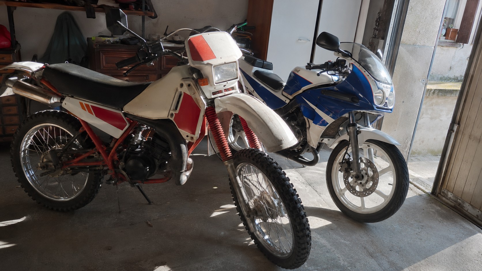 Photo réaliste de deux motos 50cc Yamaha style DT et TZR dans un garage ensoleillé, avec une mécaboîte japonaise visible, lumière naturelle, sol béton et ambiance atelier mécanique authentique