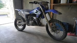 Sherco 50cc Enduro bleue et blanche dans un garage lumineux, moto tout-terrain avec pneus à crampons, cadre apparent, moteur visible et éclairage naturel intérieur.