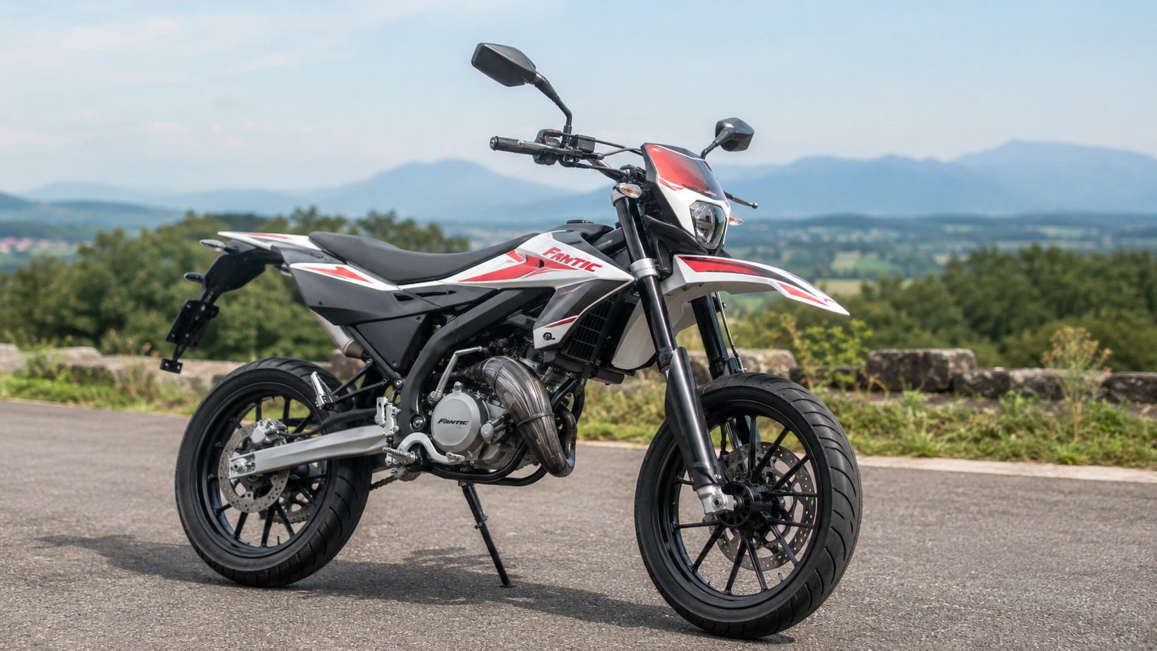 moto supermotard 50cc Fantic garée sur route panoramique, montagnes en arrière-plan