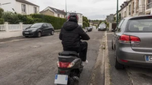 jeune_conducteur_casque_integral_blanc_rouge_doudoune_noire_scooter_50_gris_anthracite_rue_pavillonnaire_30_juillet_2026_panoramique_1672x941