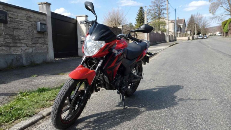 Moto 50cc de route rouge et noire stationnée dans une rue résidentielle