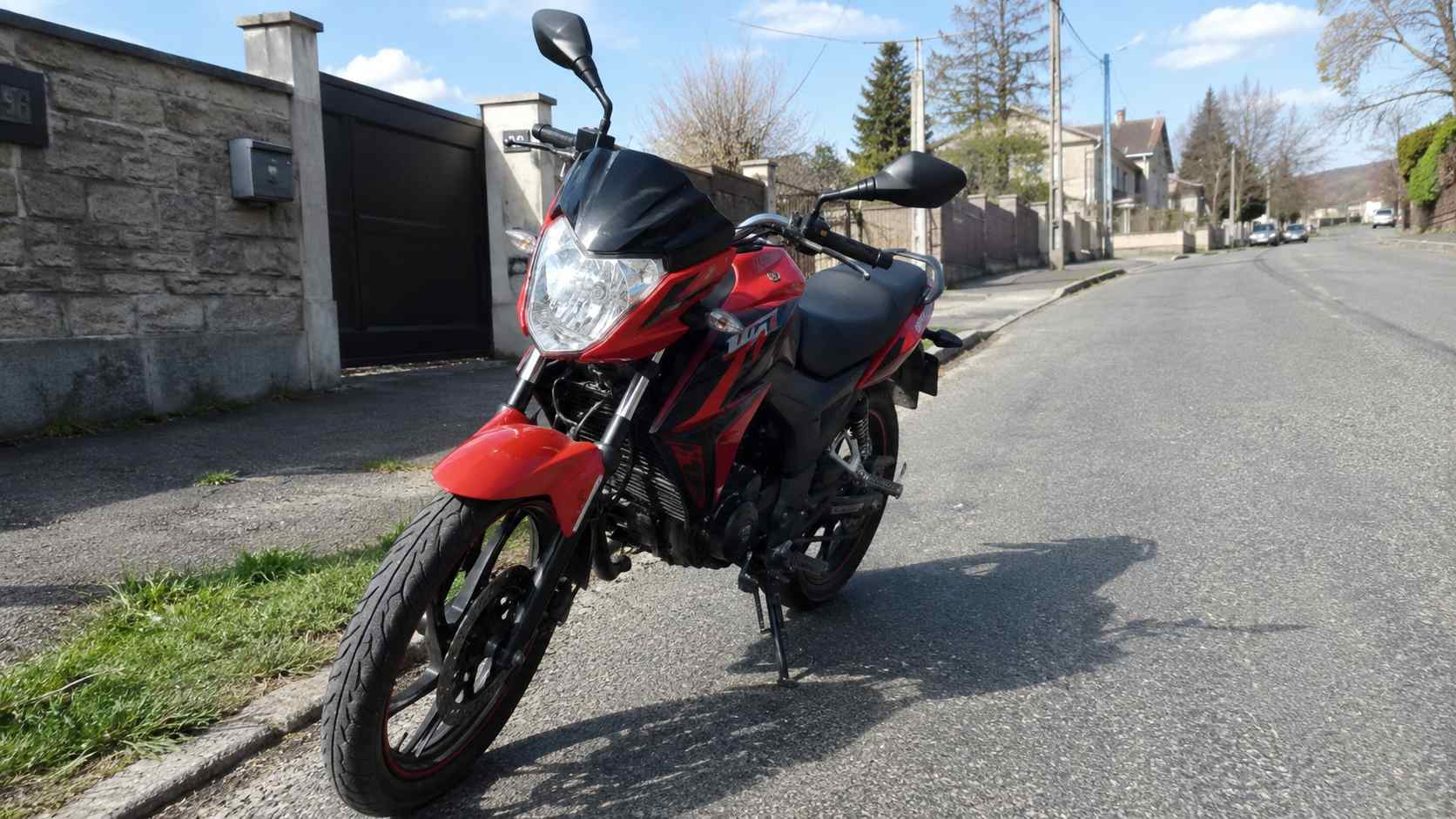 moto 50cc route rouge et noire homologuee stationnee dans une rue residentielle