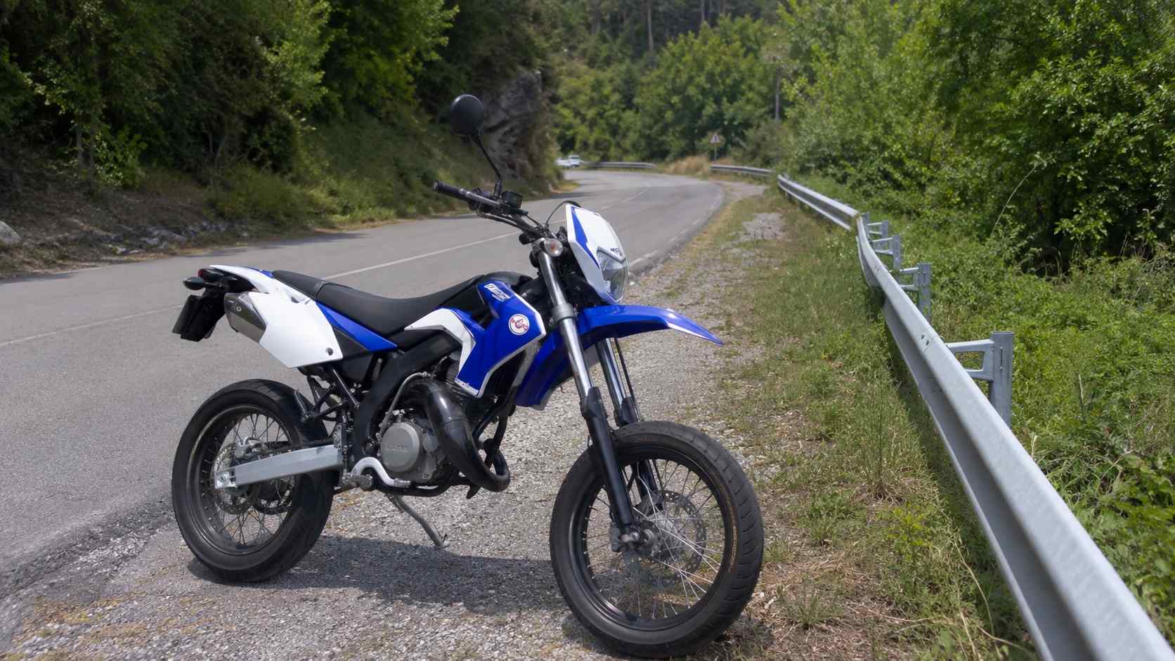 fourche inversee 50cc sur supermotard bleue et blanche sur route de campagne