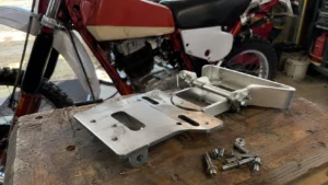 platine_support_plaque_aluminium_usine_visserie_inox_etabli_bois_moto_enduro_vintage_rouge_blanche_30_juillet_2026_panoramique_1672x941