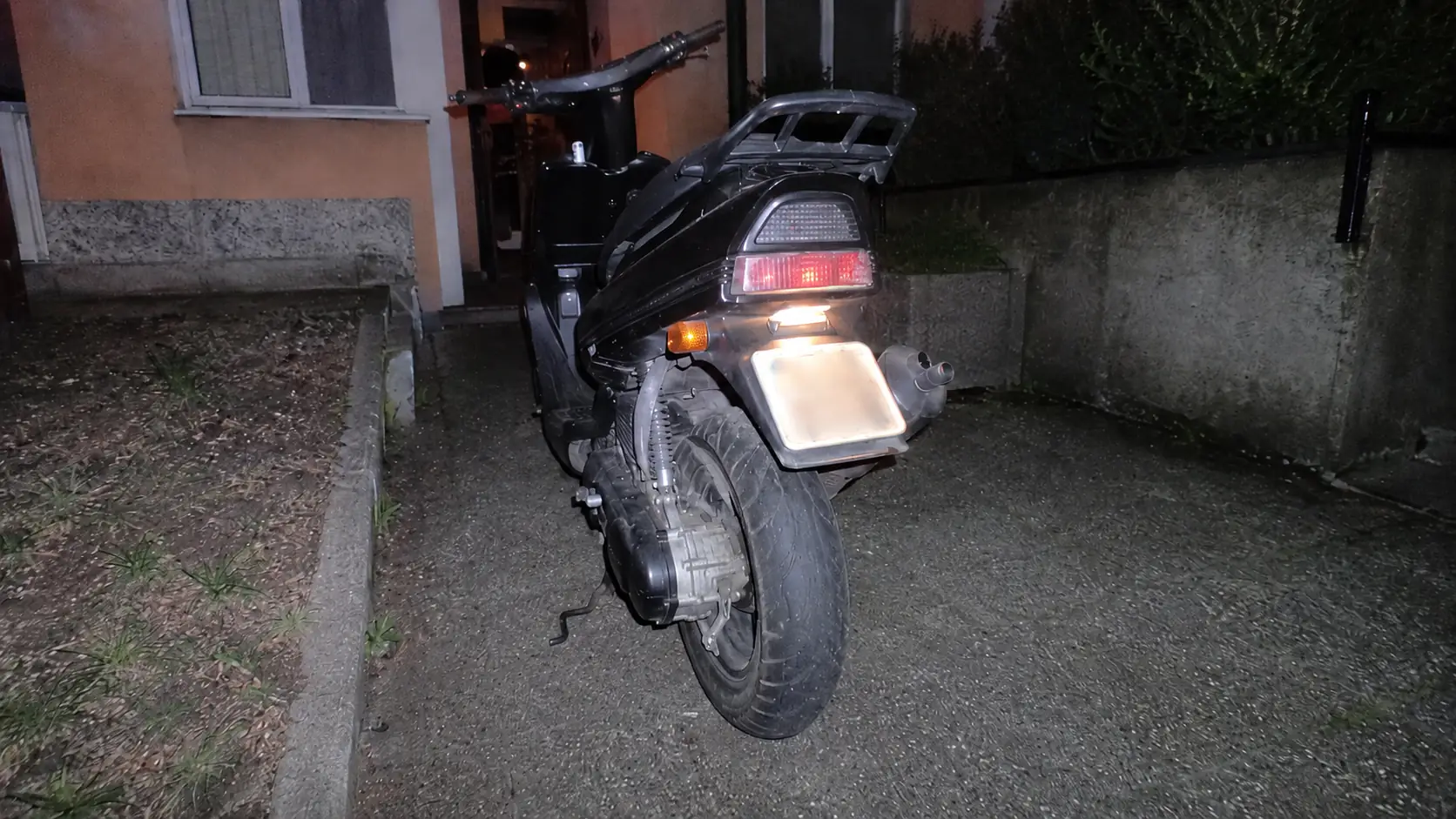 scooter 50cc noir gare de nuit avec feu arriere rouge allume et support de plaque vide