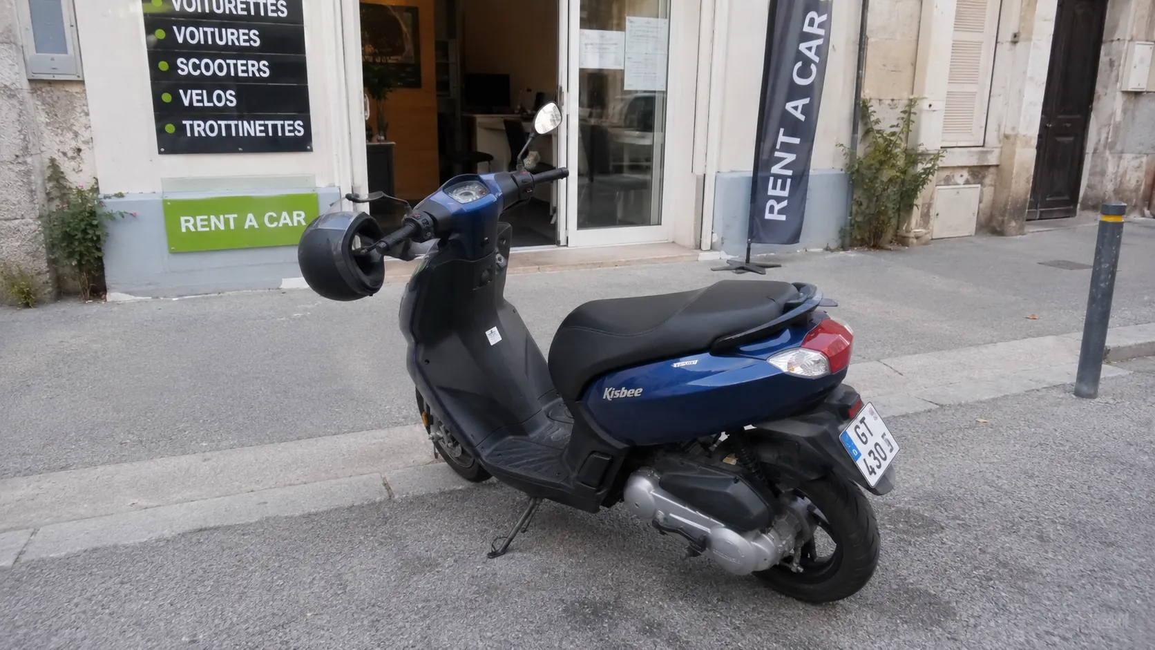 scooter 50cc Peugeot Kisbee bleu devant une agence de location scooter 50cc