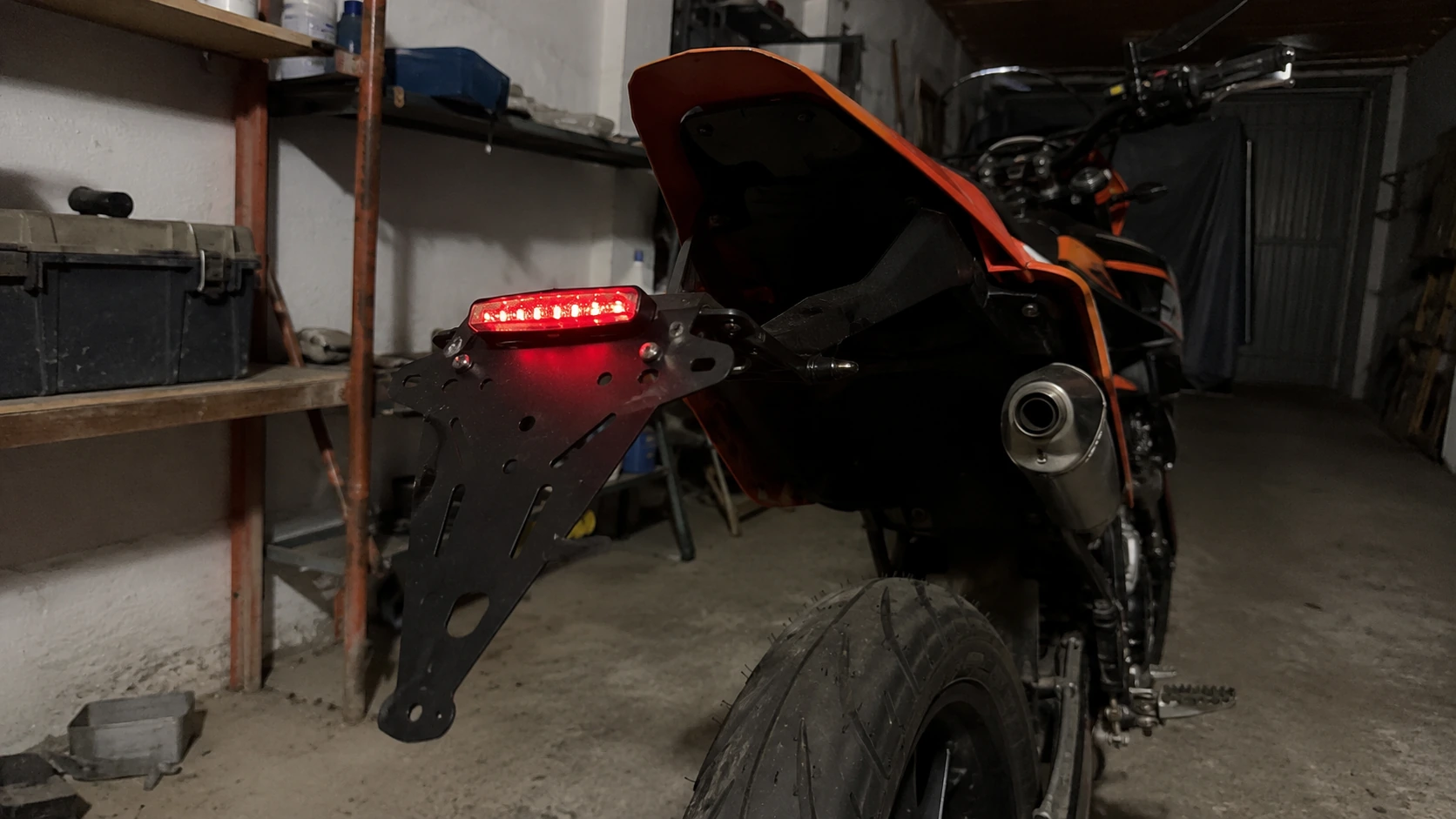 support de plaque 50cc noir ajoure avec feu led rouge allume sur supermotard orange en garage