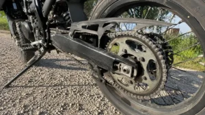 train_arriere_moto_50_bras_oscillant_noir_couronne_acier_chaine_tendeur_disque_frein_jante_rayons_contre_plongee_30_juillet_2026_panoramique_1672x941