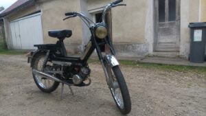 Mobylette 50cc noire style Motobécane vintage moteur thermique monocylindre refroidissement air échappement chromé roues rayons freins tambour fourche télescopique suspensions arrière cour maison campagne française