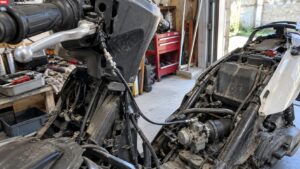 Scooter 50cc démonté dans un atelier, câble d’accélérateur visible entre la poignée droite et le carburateur, gaine noire avec tendeur de réglage, carénages retirés, moteur et admission accessibles pour diagnostic et réglage