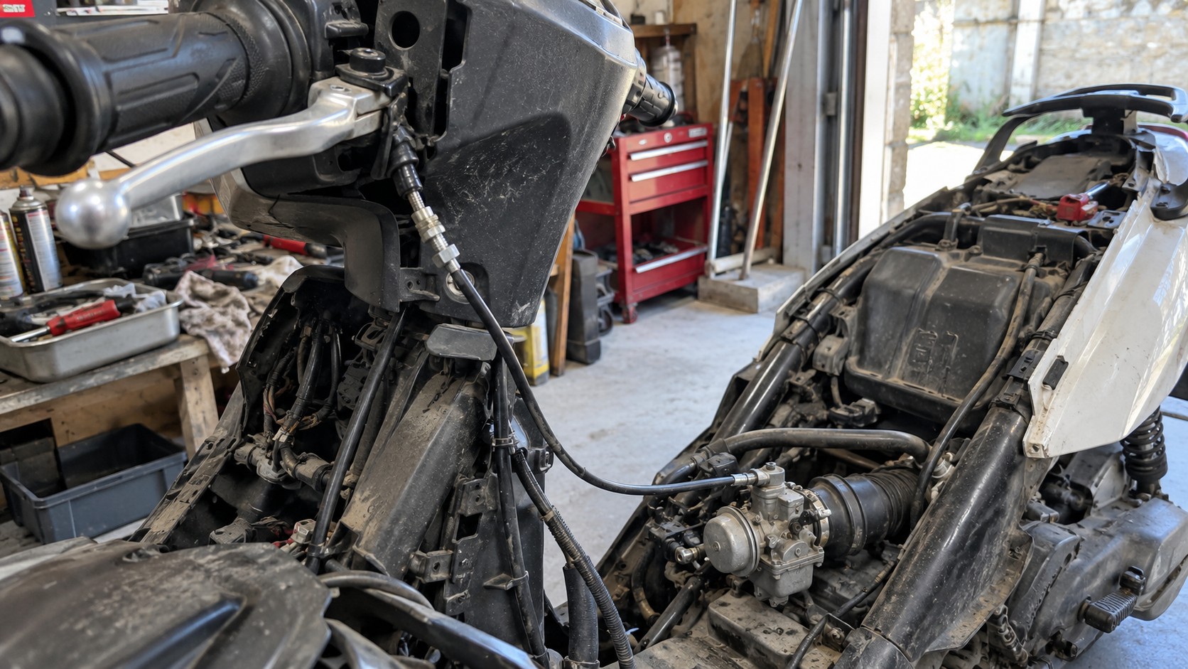Scooter 50cc démonté dans un atelier, câble d’accélérateur visible entre la poignée droite et le carburateur, gaine noire avec tendeur de réglage, carénages retirés, moteur et admission accessibles pour diagnostic et réglage