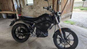 Super Soco TC électrique noire, vue latérale droite, garée dans une grange aux murs en pierre