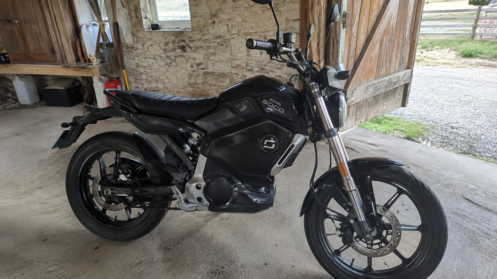 Super Soco TC électrique noire, vue latérale droite, garée dans une grange aux murs en pierre